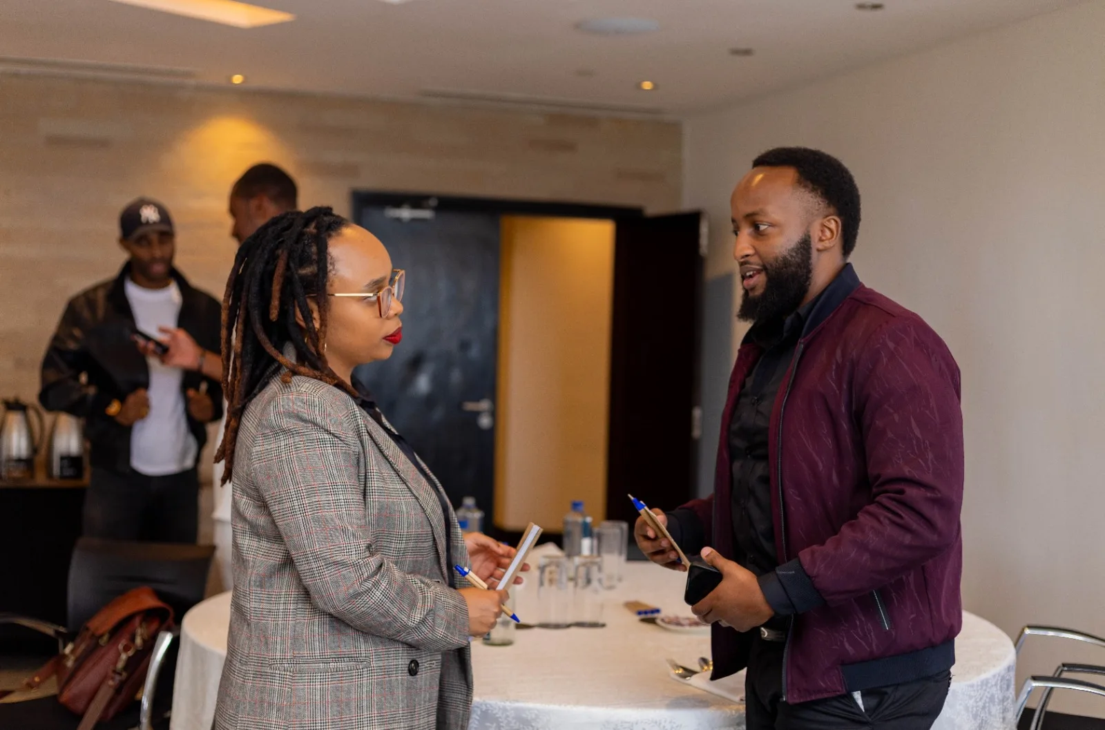 Two guests holding notebooks and talking beside a table at a Chamber event